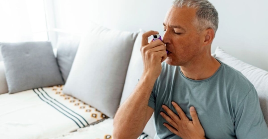 man sitting on couch using an inhaler