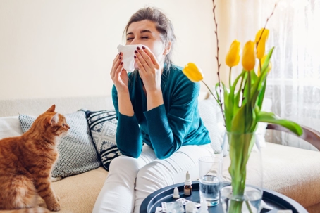 woman sneezing next to cat and flowers